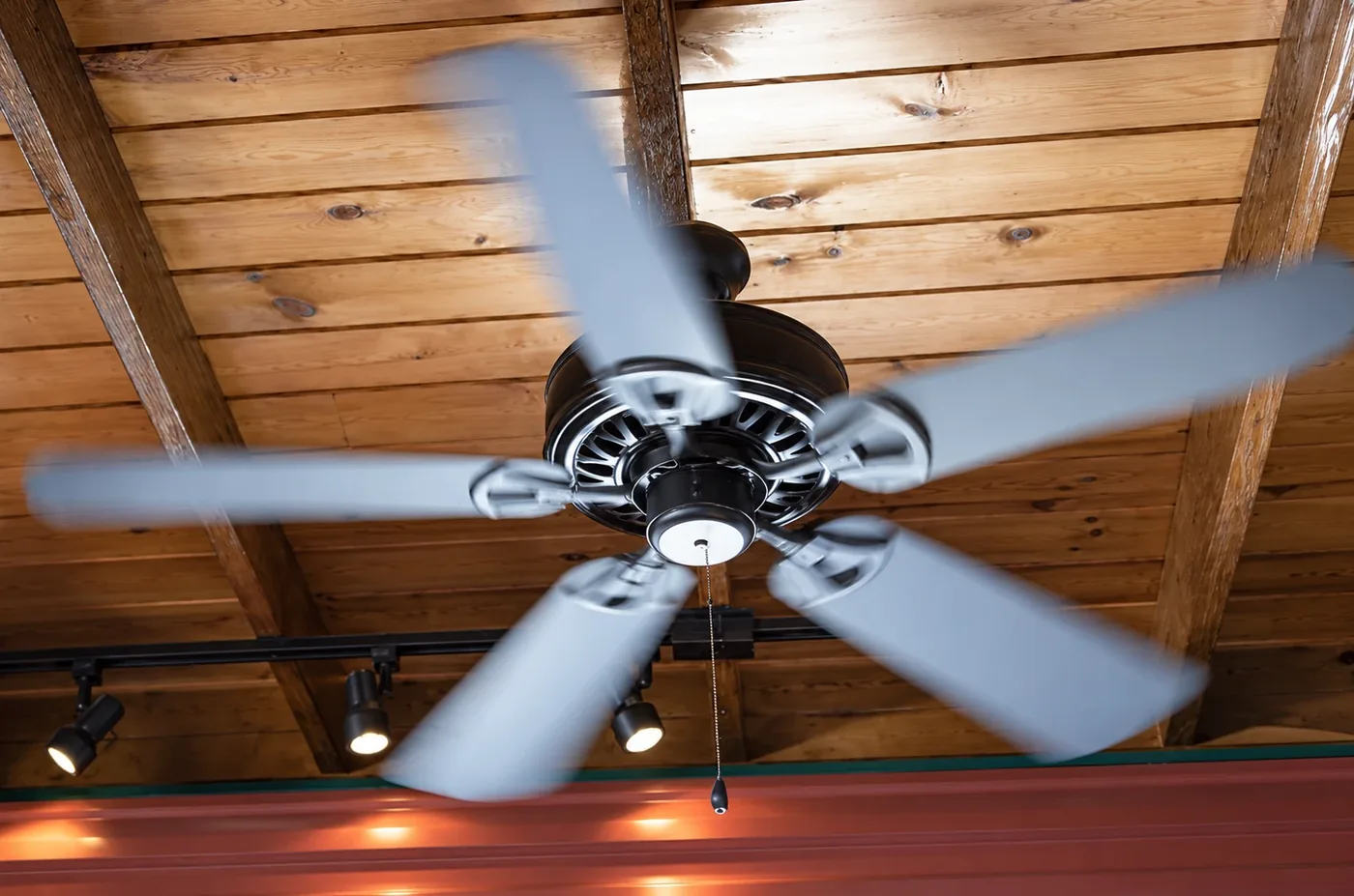 Ceiling fan spinning smoothly on a wood-beam ceiling with track lighting, installed by AllPro AG in San Diego