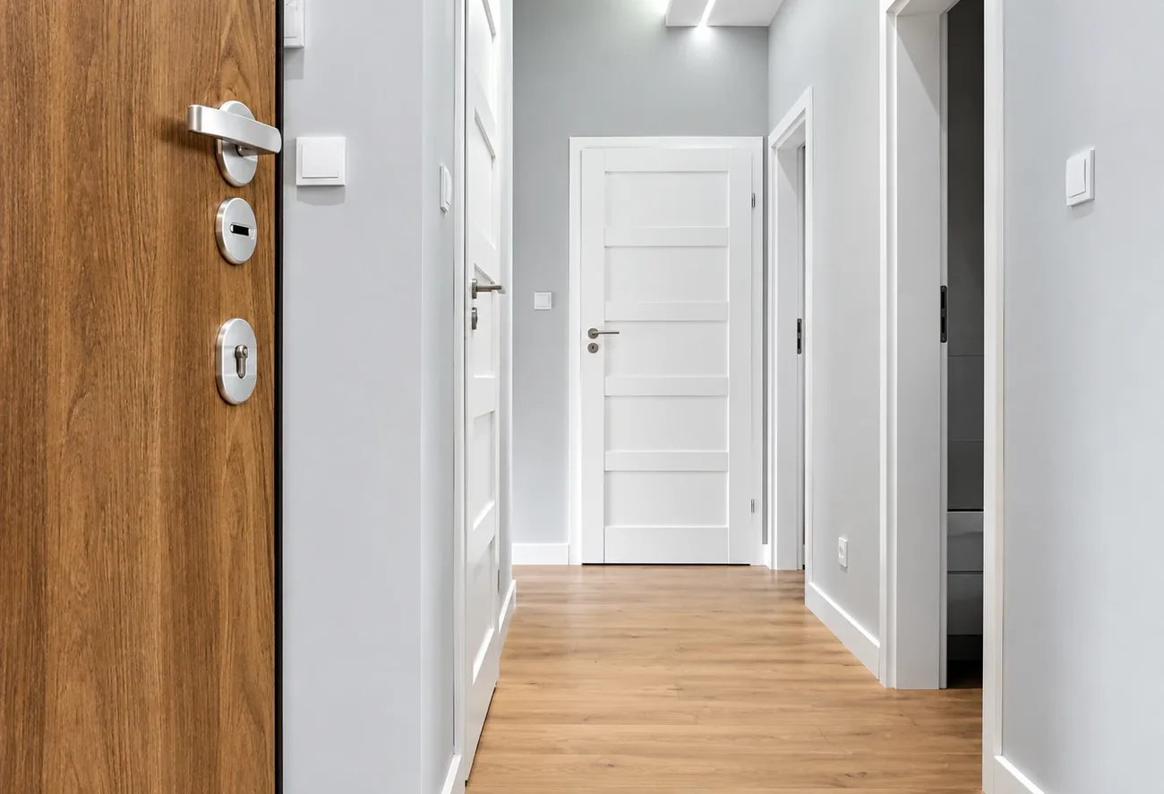 Bright hallway with a solid wood entry door, stainless lever handle and deadbolts, leading to white panel interior doors, serviced by AllPro AG in San Diego