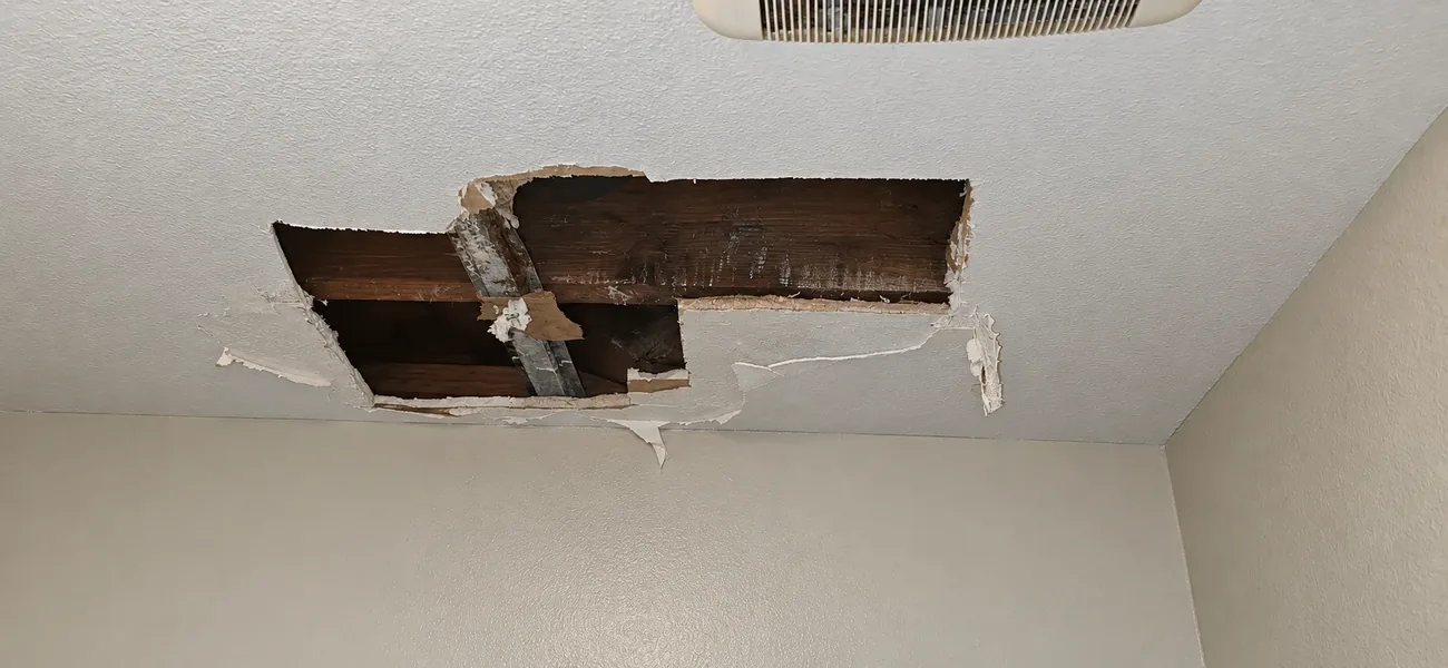 Water-damaged ceiling with a broken-out section exposing the joists, ready for drywall repair by AllPro AG in San Diego