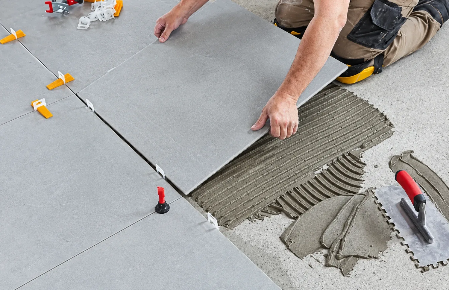 AllPro AG installer setting large-format gray floor tile into notched mortar with leveling clips on a San Diego floor