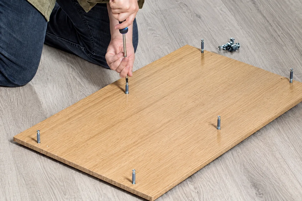 AllPro AG technician driving cam-lock fasteners into an oak panel during flat-pack furniture assembly in San Diego