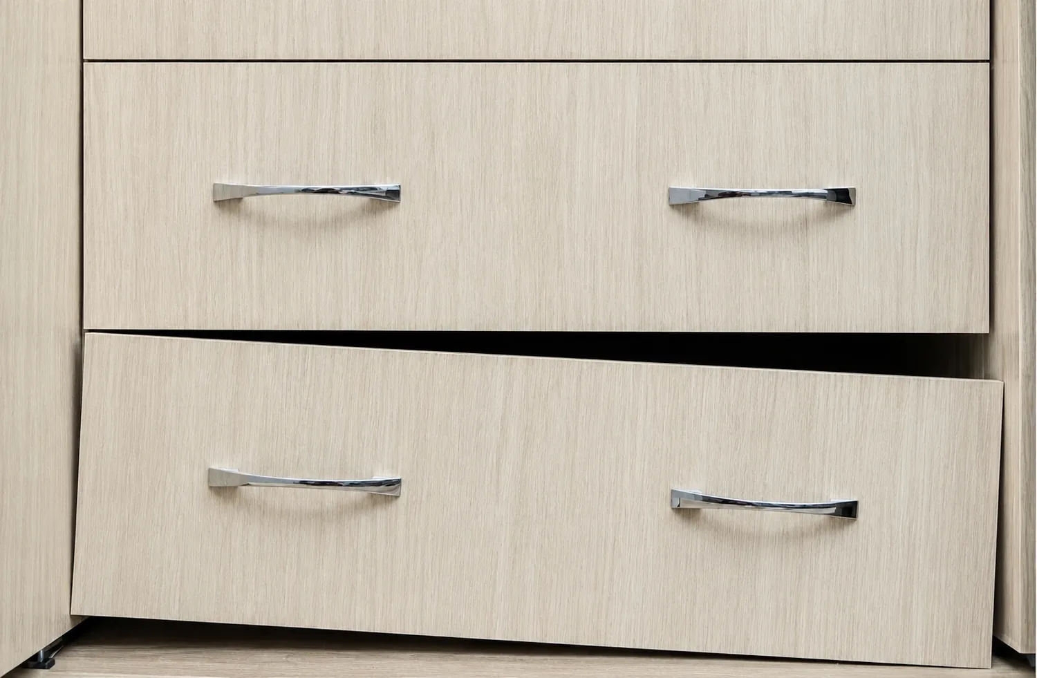 Light oak dresser drawer sagging crooked off its slide below a closed drawer with chrome pulls, ready for drawer track repair in San Diego