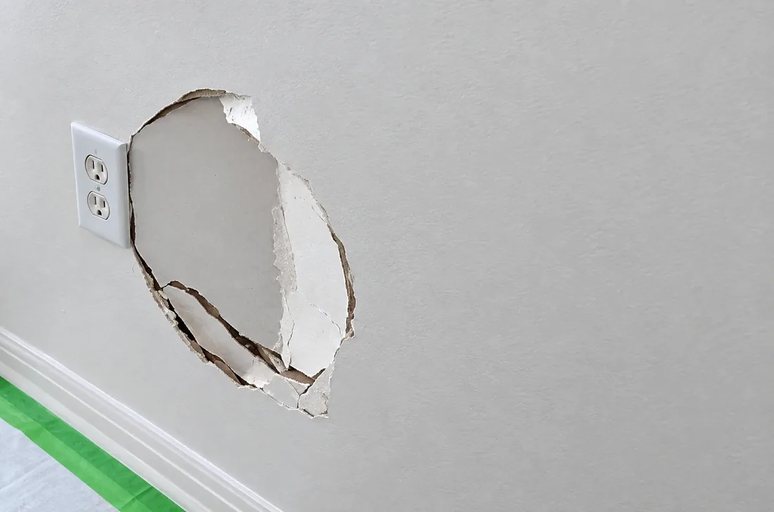 AllPro AG drywall repair, a broken hole in a wall beside an outlet ready to be patched, in a San Diego home